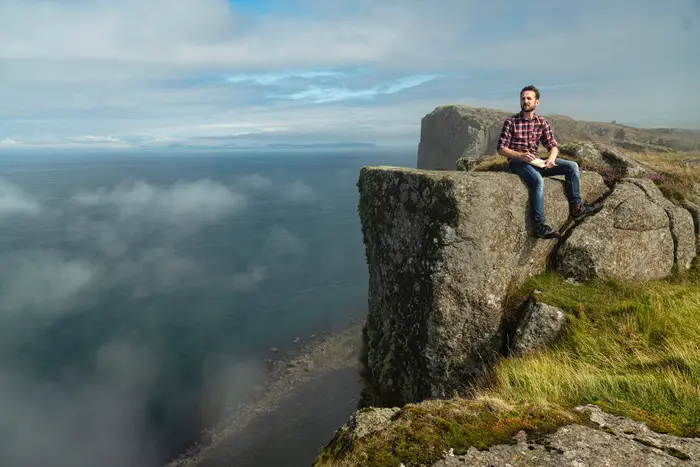 a man on a cliff with the sky in the background